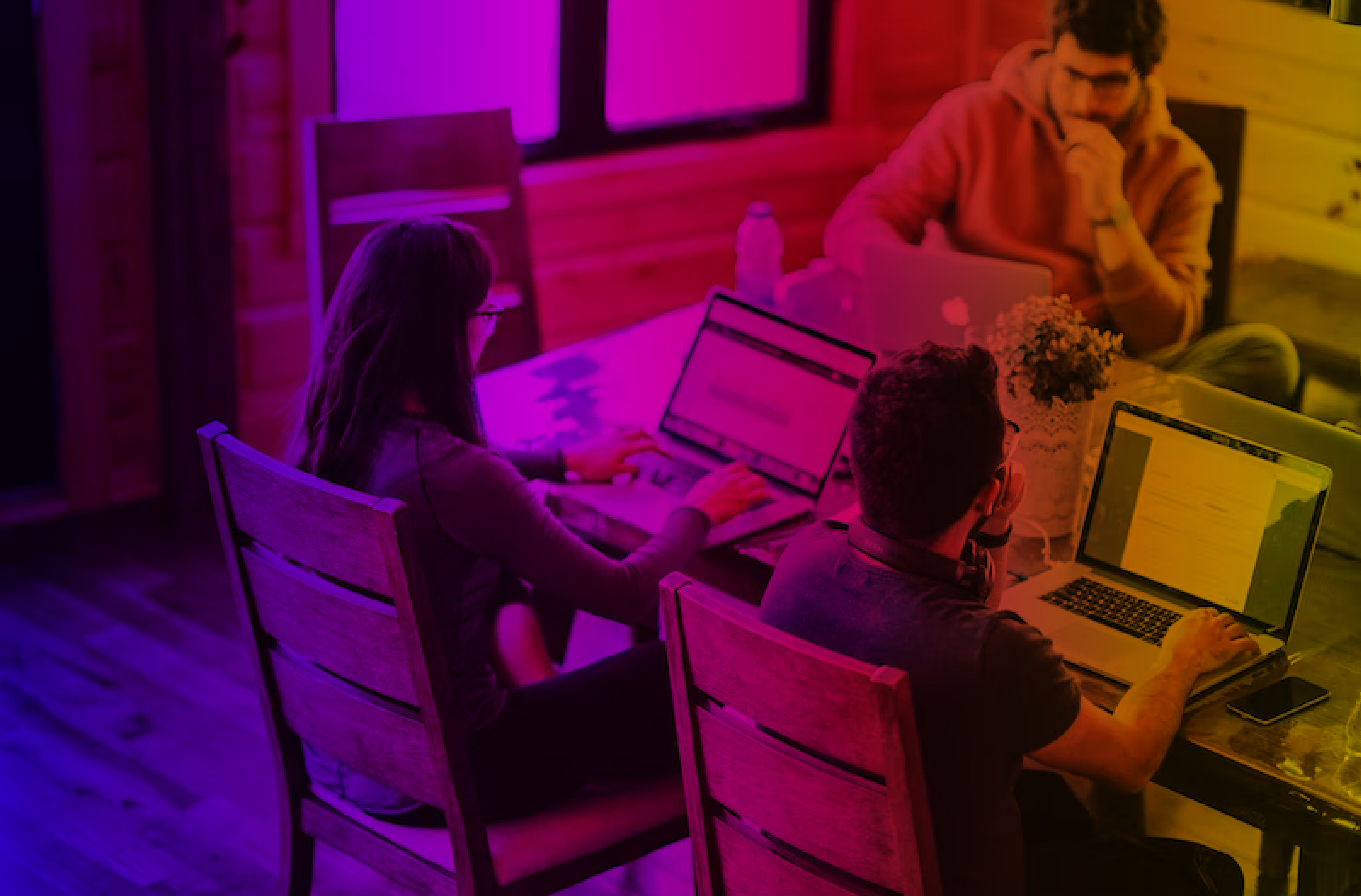 Three people focused on laptops at a table with a purple and orange color overlay.